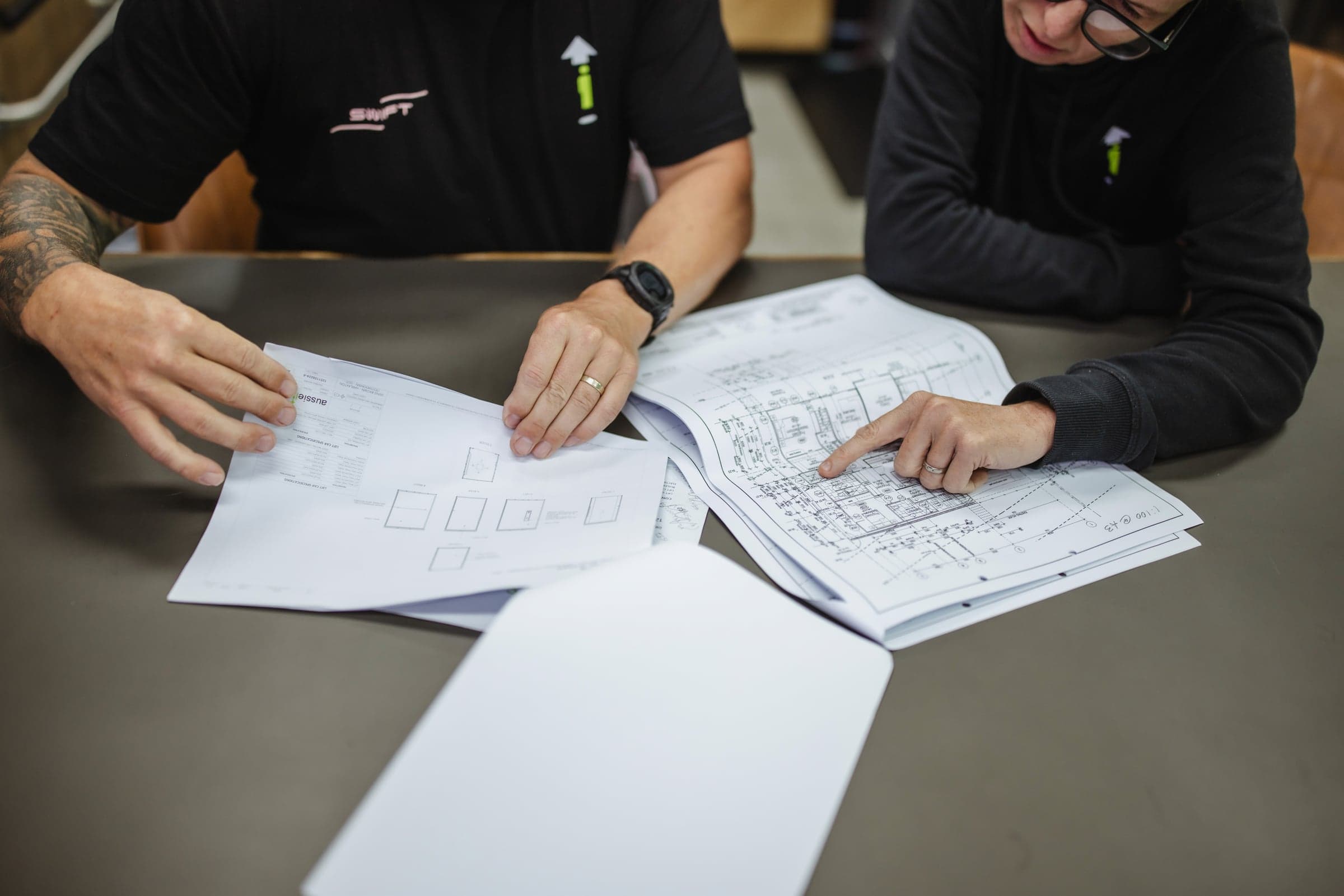 Close-up of two people pointing at printed lift layout drawings spread on a table