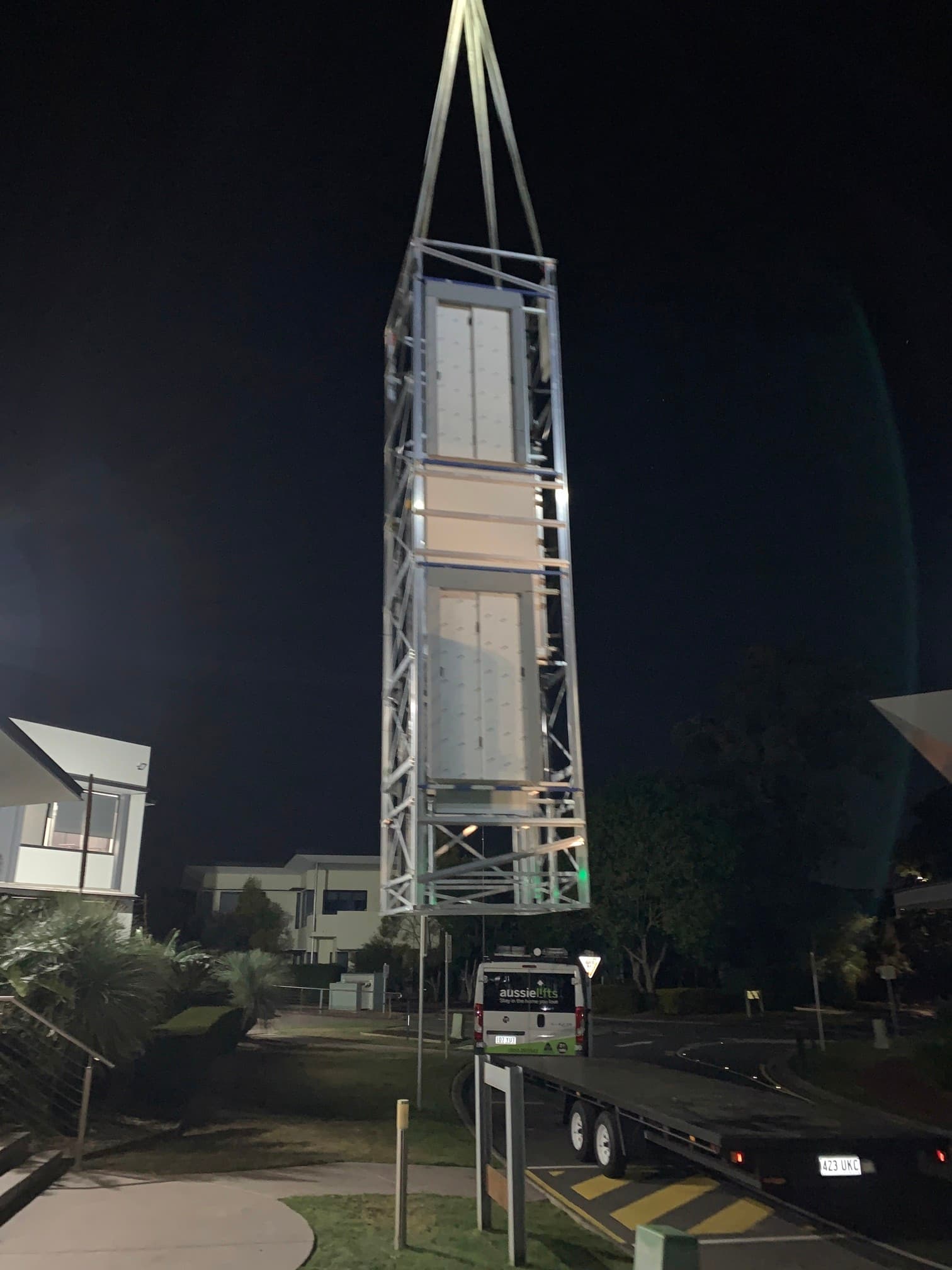 Lift shaft with two landing doors being craned off a truck trailer at night, a van parked below