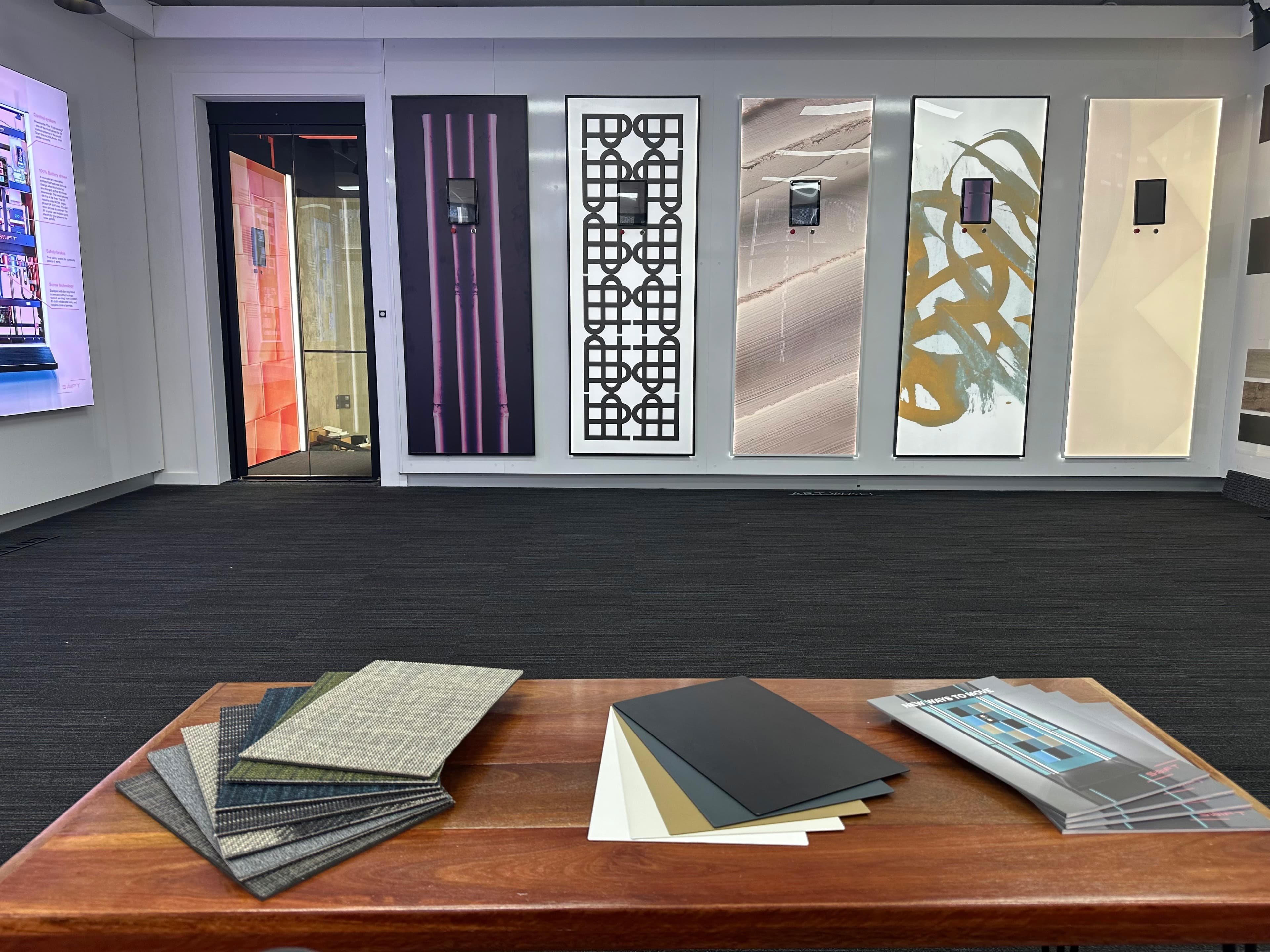 Aussie Lifts Sydney showroom at Banksmeadow, a row of lift wall panel designs behind a table of floor and finish samples