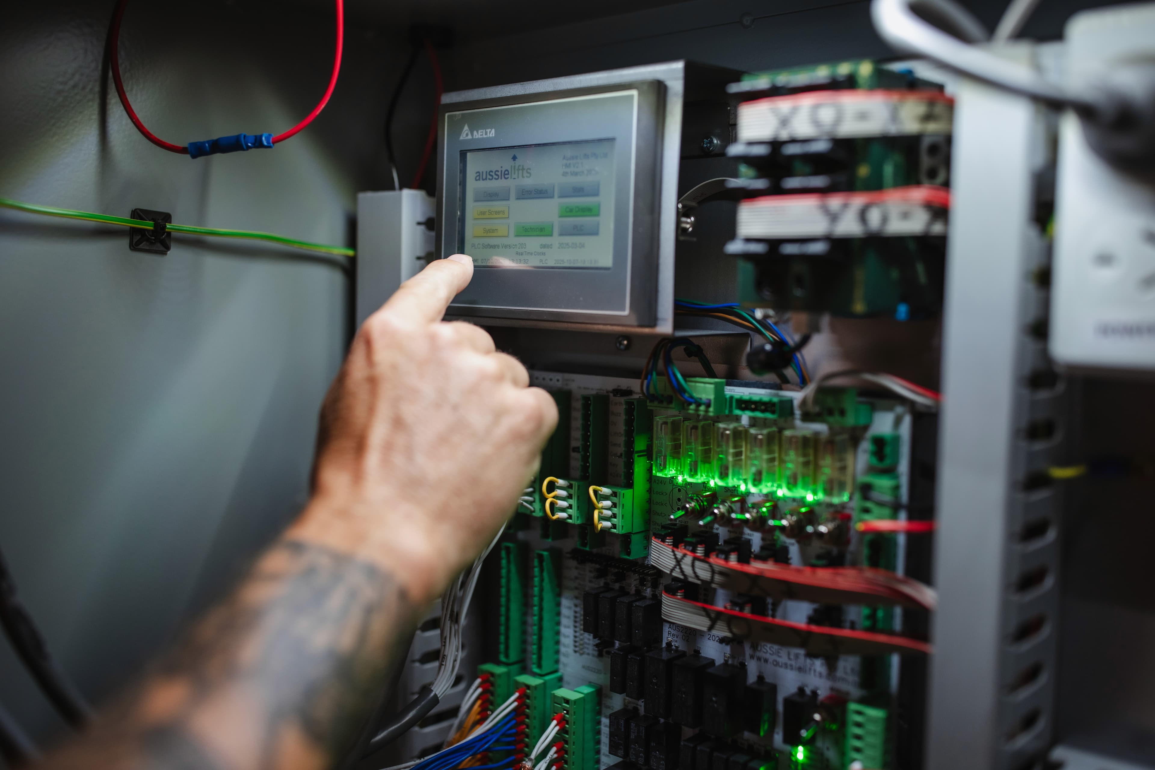 Technician using the touchscreen on an Aussie Lifts controller in an open control cabinet